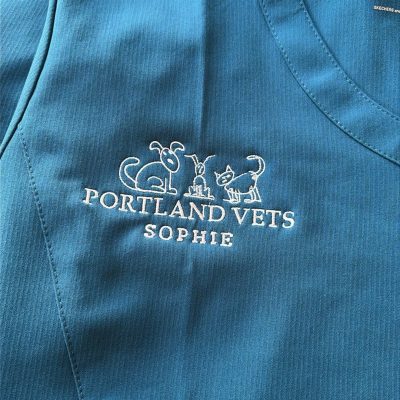 Blue embroidered veterinary scrub top for Portland Vets with custom white logo and Sophie name embroidery by KMVT Workwear